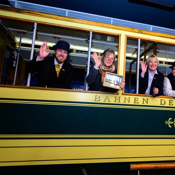 Vier Personen gucken und winken aus einer alten Straßenbahn.