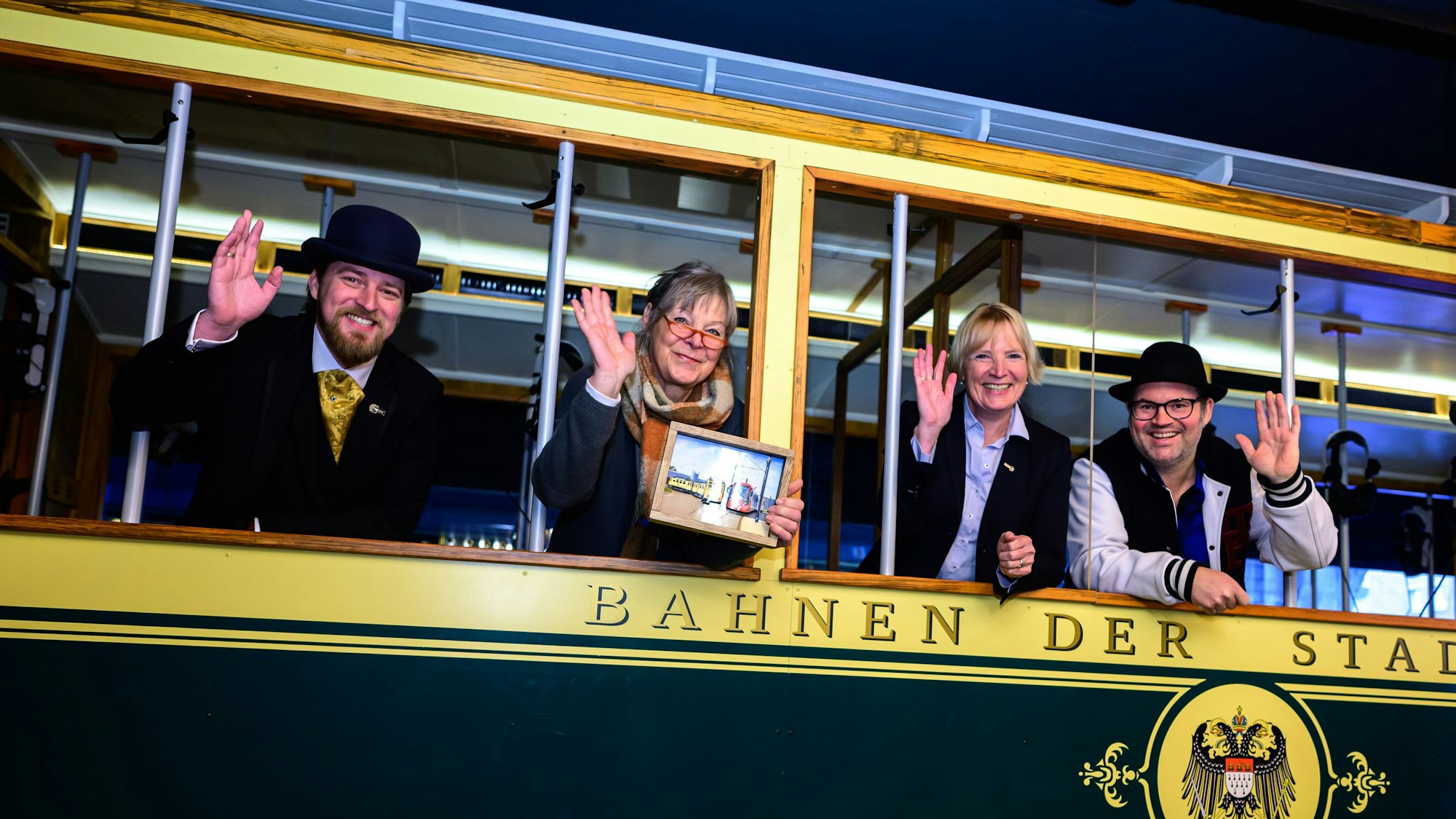 Vier Personen gucken und winken aus einer alten Straßenbahn.