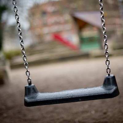 Auf dem Foto ist ein Spielplatz mit einer Schaukel im Vordergrund zu sehen.