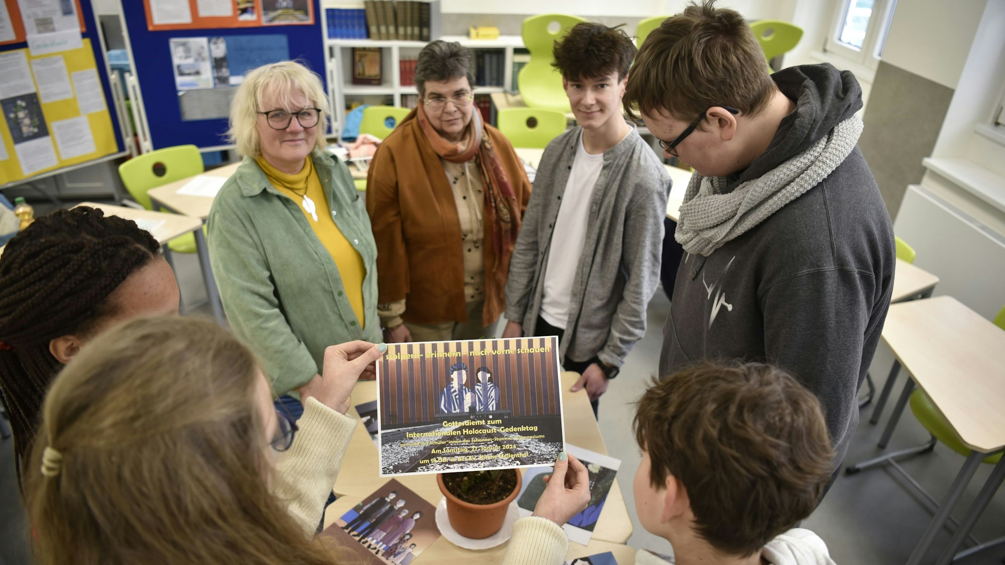 Schülerinnen und Schüler stehen im Kreis um einen Tisch mit verschiedenen Zeichnungen. Ein Mädchen hält ein Plakat in die Kamera.