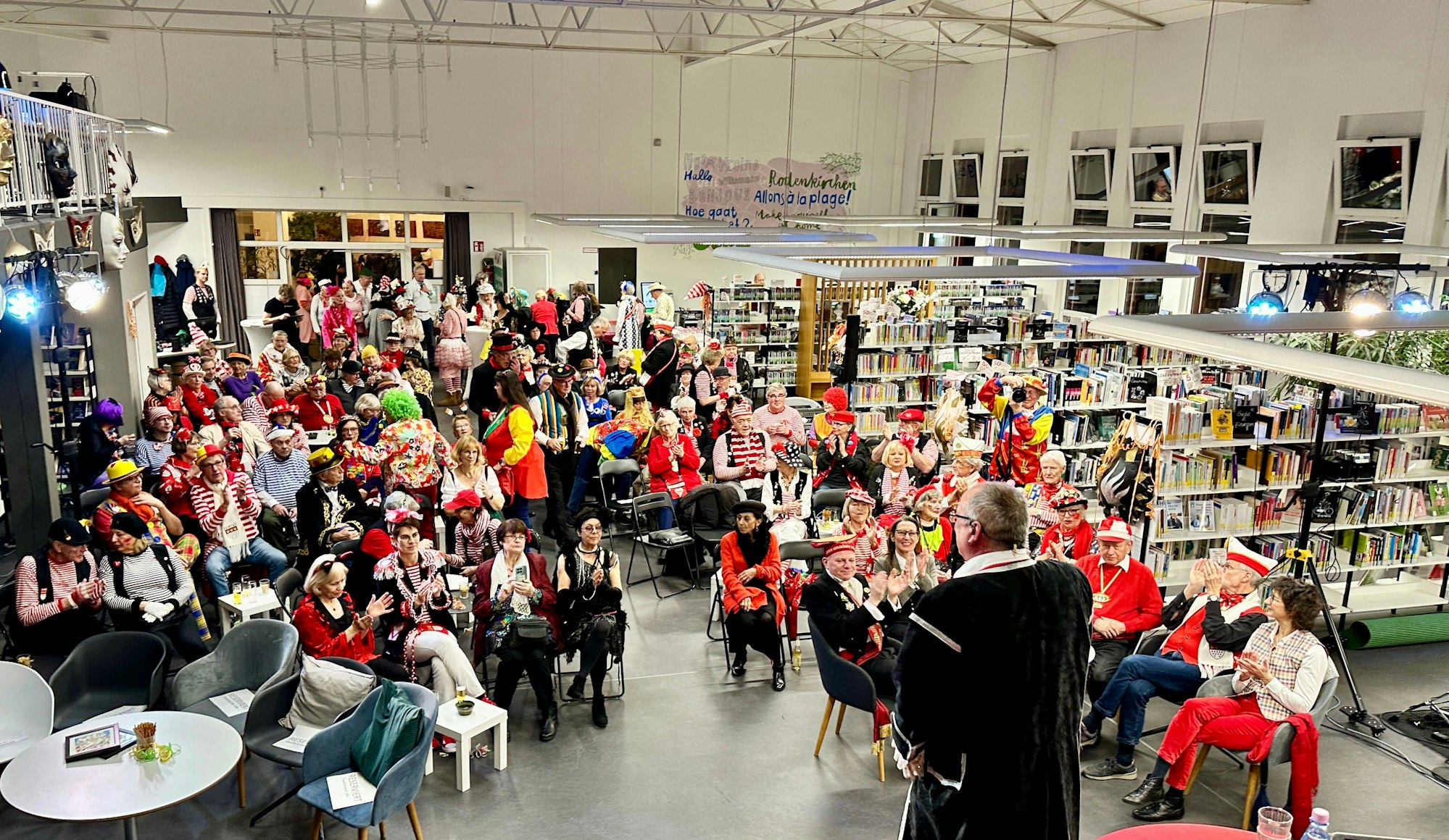 Blick in einen großen Raum mit Bücherregalen und vielen von bunt kostümierten Gästen besetzten Stuhlreihen