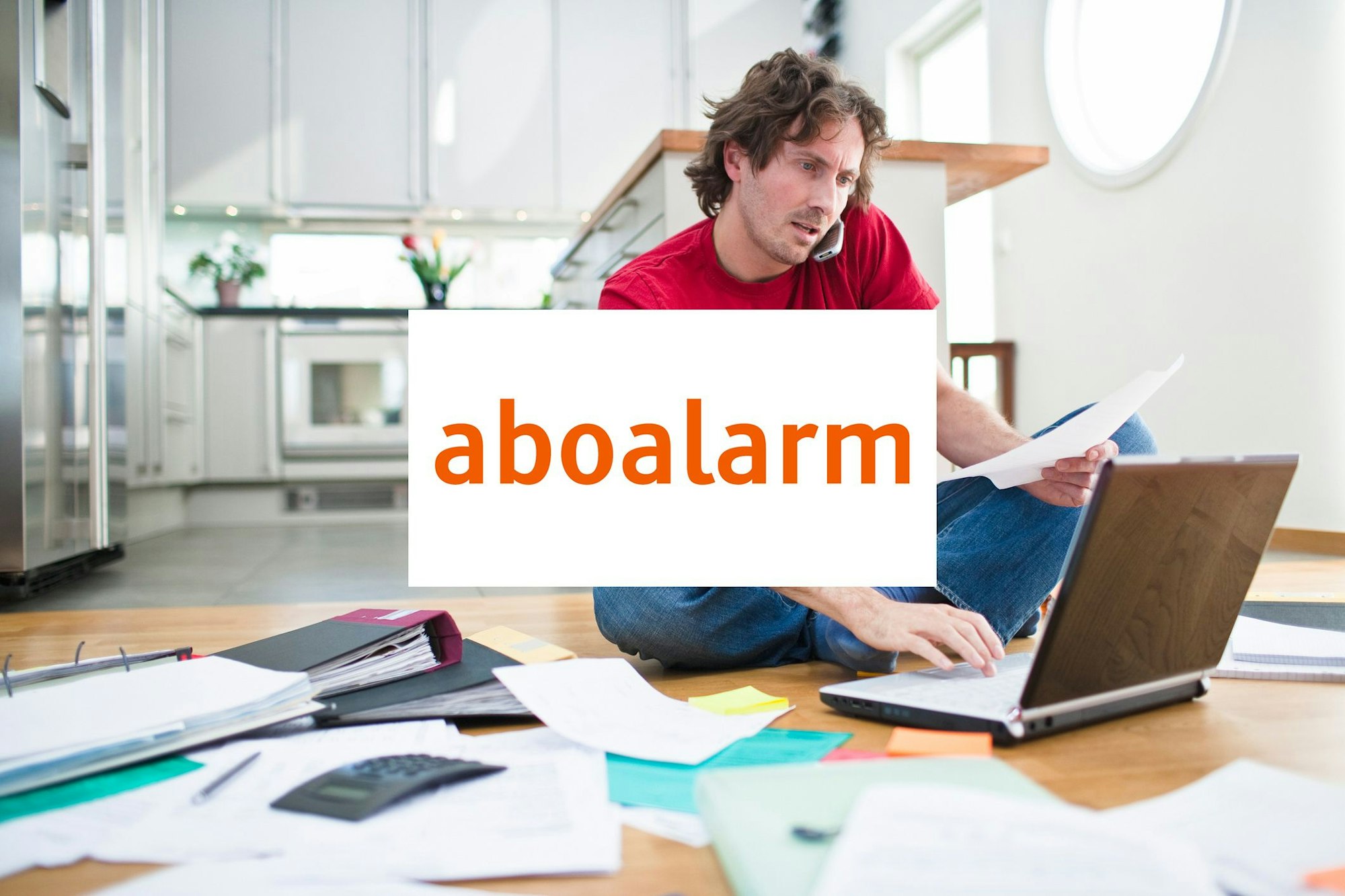 Mann sitzt an seinem Laptop auf dem Boden und um ihn herum liegen Papierstapel. Logo von Aboalarm in der Bildmitte