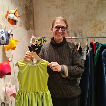 Eine Frau steht in einem Laden, sie zeigt ein grünes Kleid.