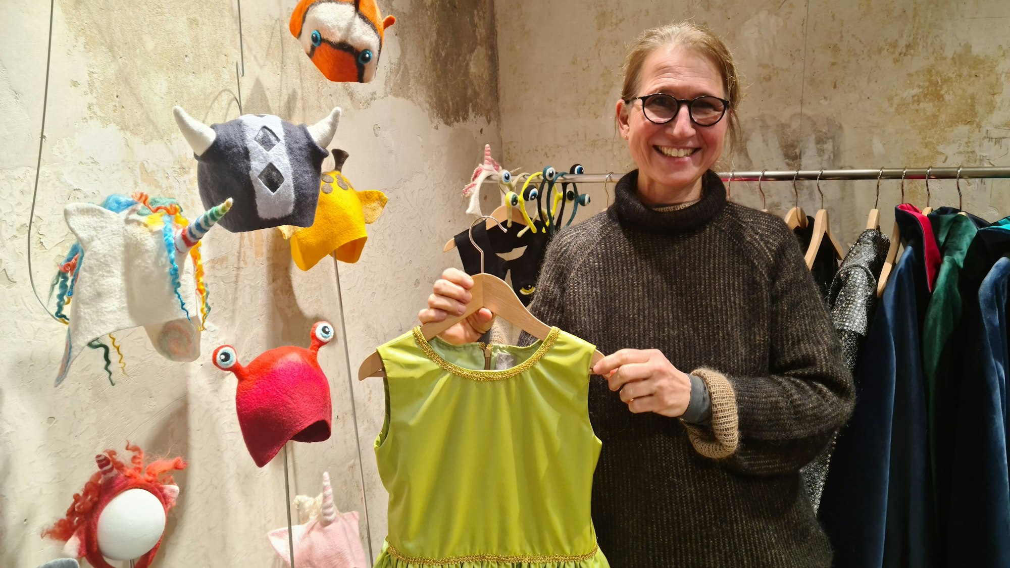 Eine Frau steht in einem Laden, sie zeigt ein grünes Kleid.