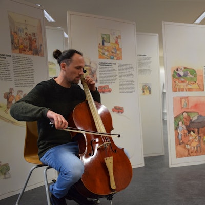 Ein Cello-Spieler sitzt vor Aufstellern.