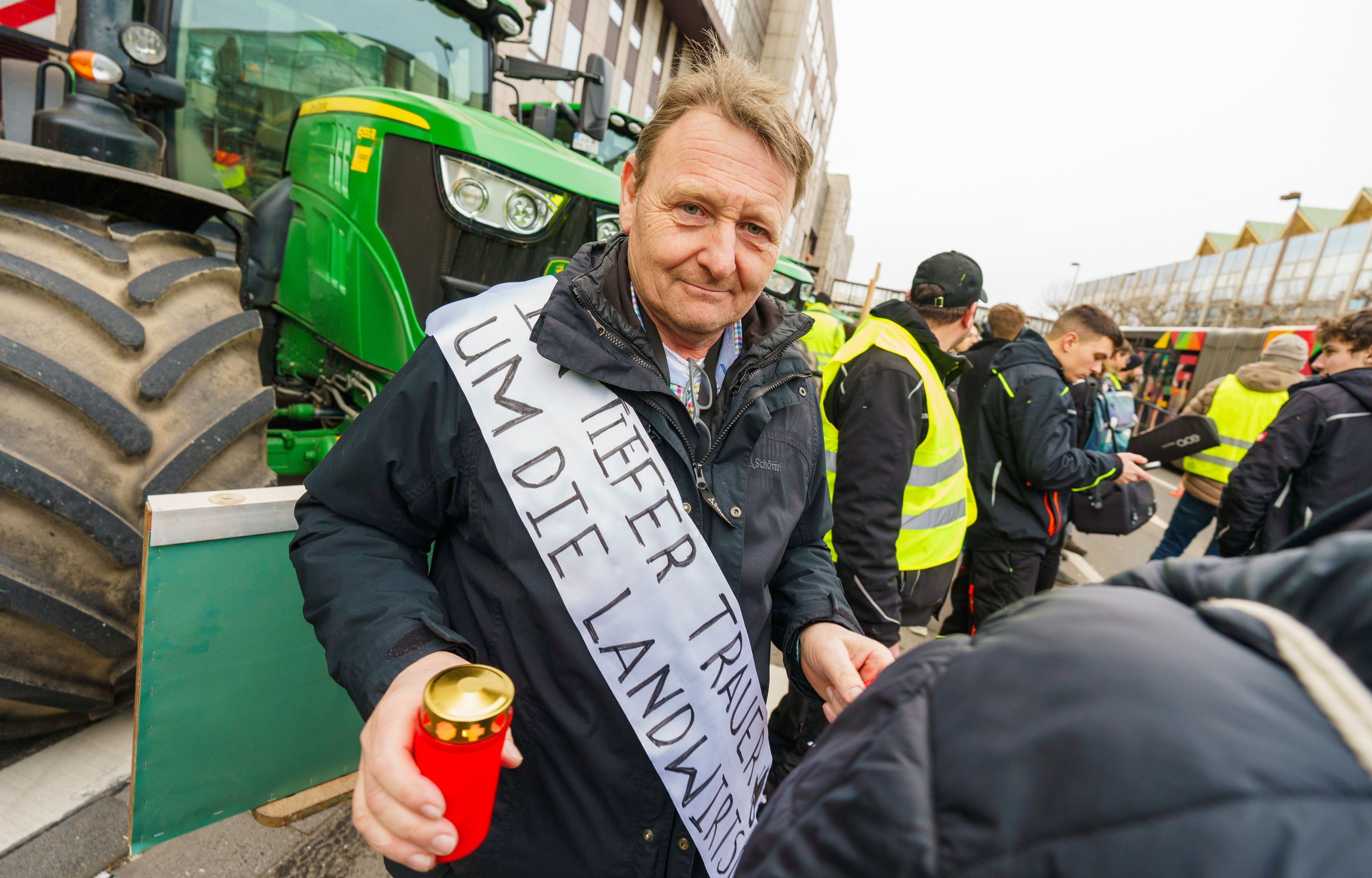 Ein Landwirt trägt auf einer Demonstration vor der Rheingoldhalle in Mainz eine Schärpe mit der Aufschrift „In tiefer Trauer um die Landwirtschaft“ über der Schulter.