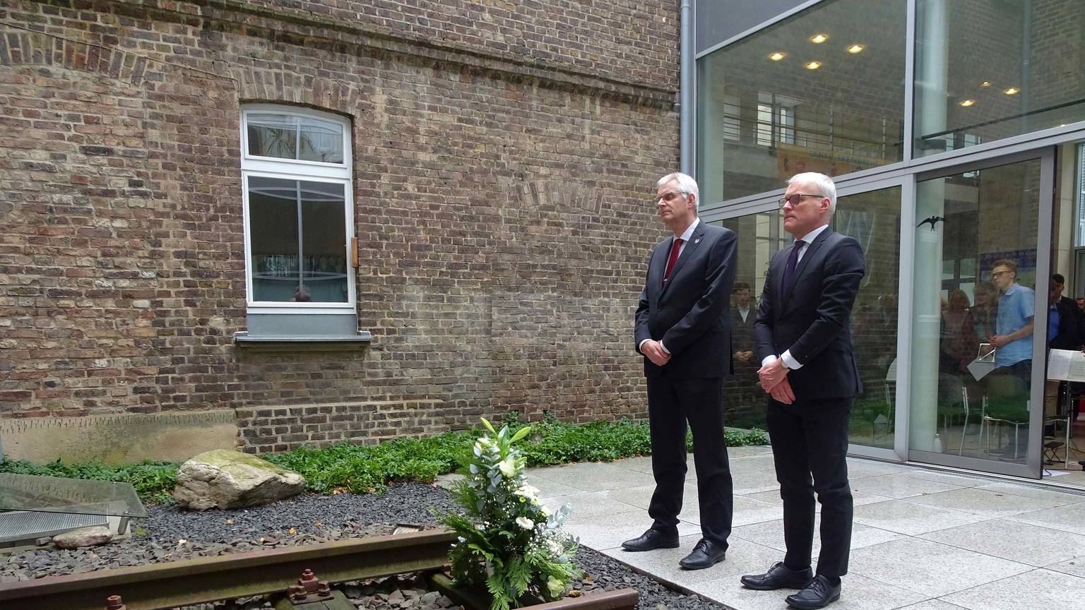 Rheinbachs Bürgermeister Ludger Banken und der Landtagsabgeordnete Oliver Krauß legen ein Gesteck im Innenhof des Rheinbacher Rathauses nieder, vor einer Gedenkstätte der Opfer des Nationalsozialismus.