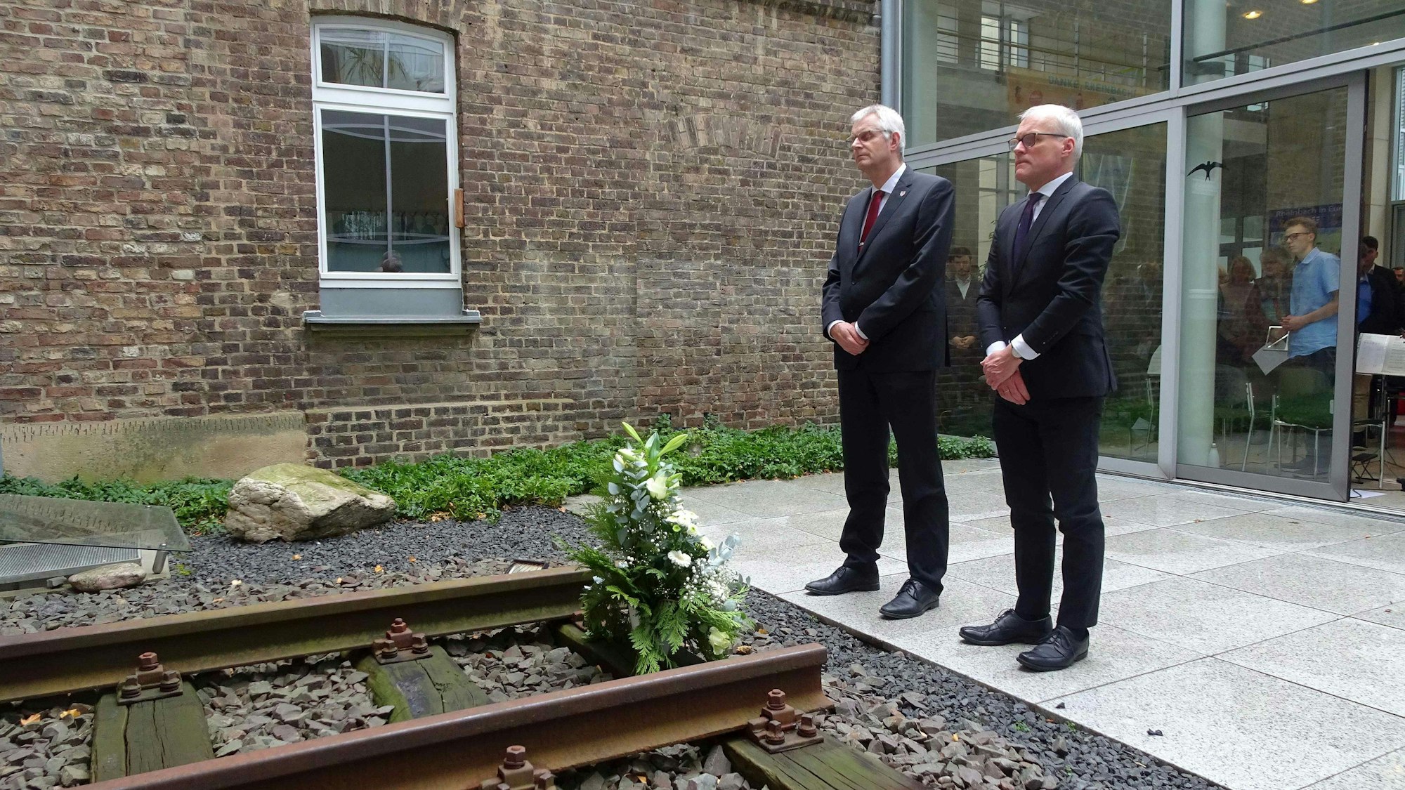 Rheinbachs Bürgermeister Ludger Banken und der Landtagsabgeordnete Oliver Krauß legen ein Gesteck im Innenhof des Rheinbacher Rathauses nieder, vor einer Gedenkstätte der Opfer des Nationalsozialismus.