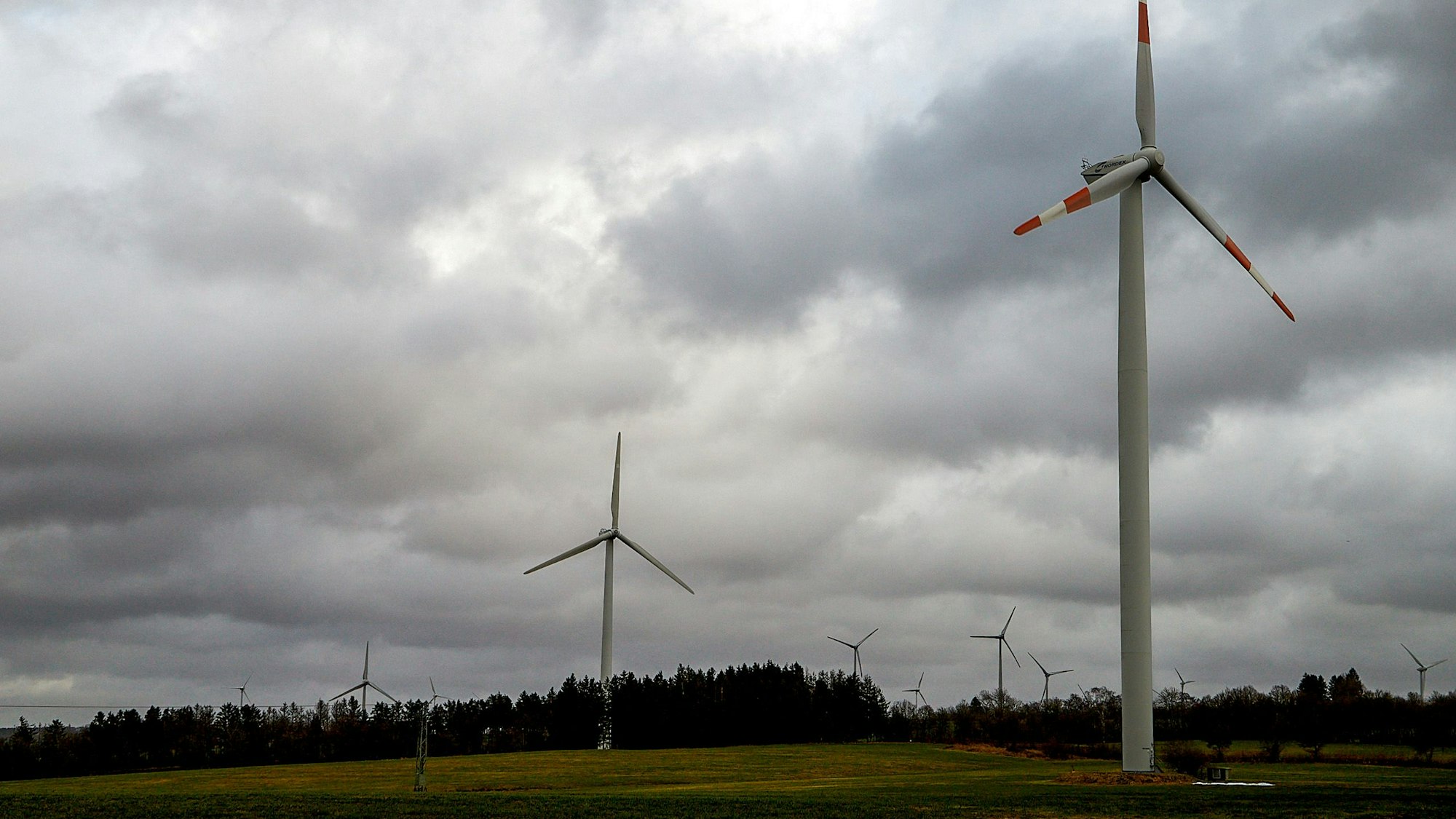 Mehrere Windräder an der Landesgrenze zwischen NRW und Rheinland-Pfalz vor wolkenverhangenem Himmel.