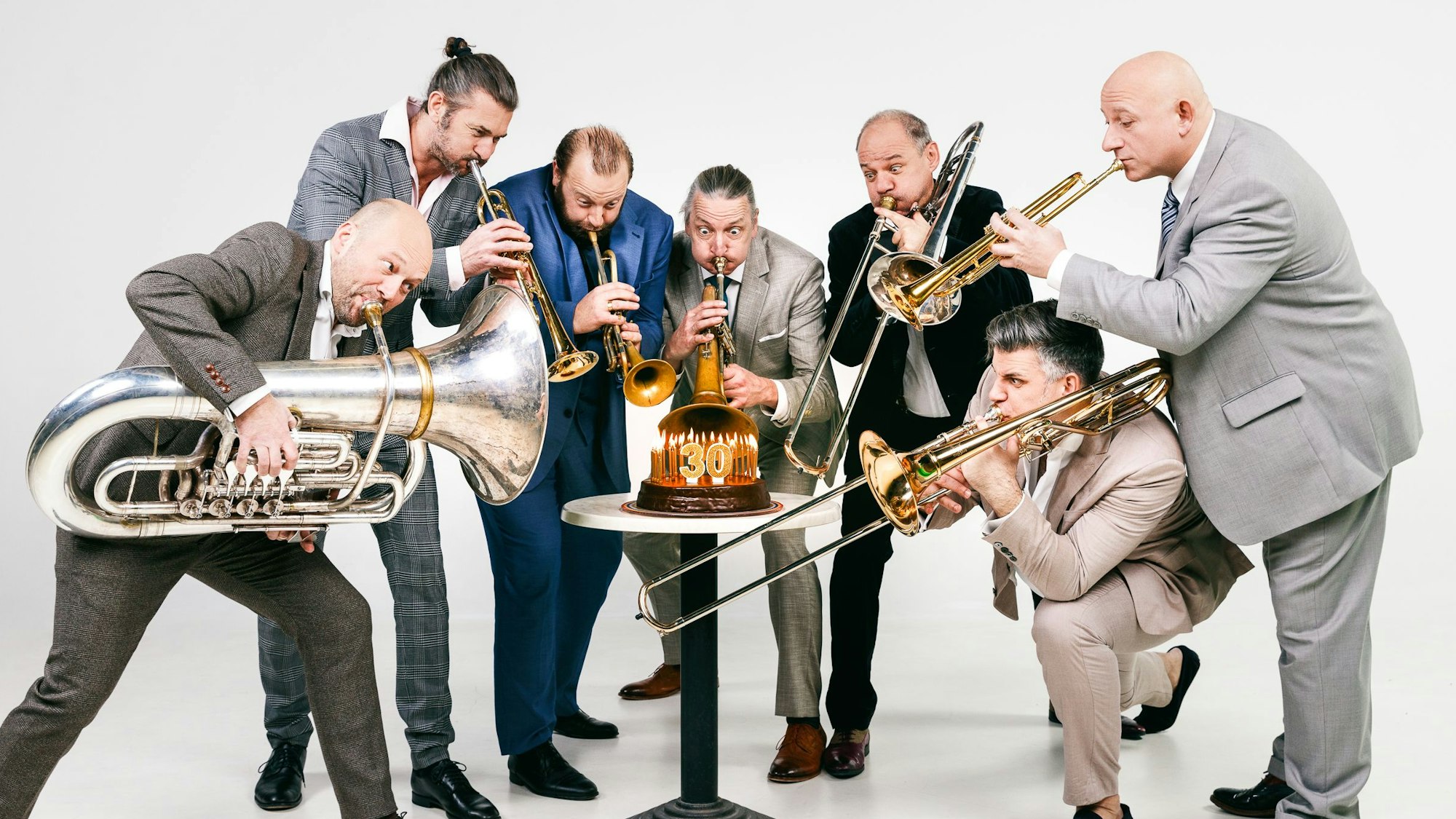 Die Mitglieder von Mnozil Brass spielen ihre Instrumente. Zwischen ihnen steht ein Kuchen.