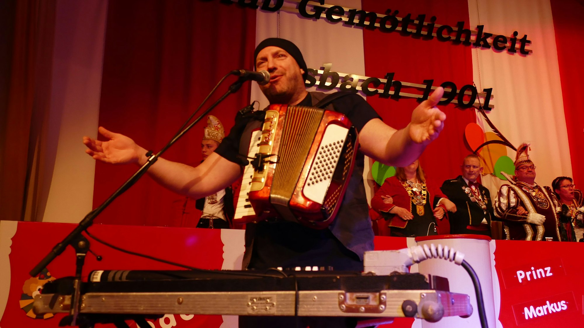 Ein Mann mit einem Akkordeon steht auf einer Karnevalsbühne.