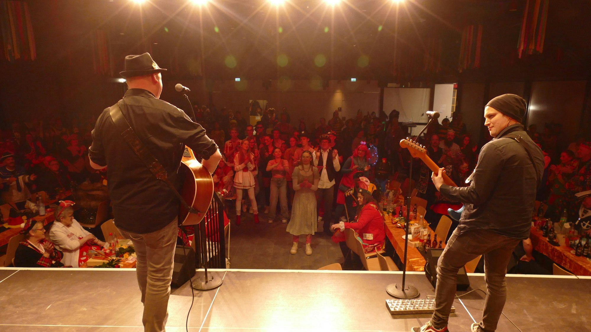 Zwei Musiker stehen auf der Bühne und werden von hinten fotografiert.