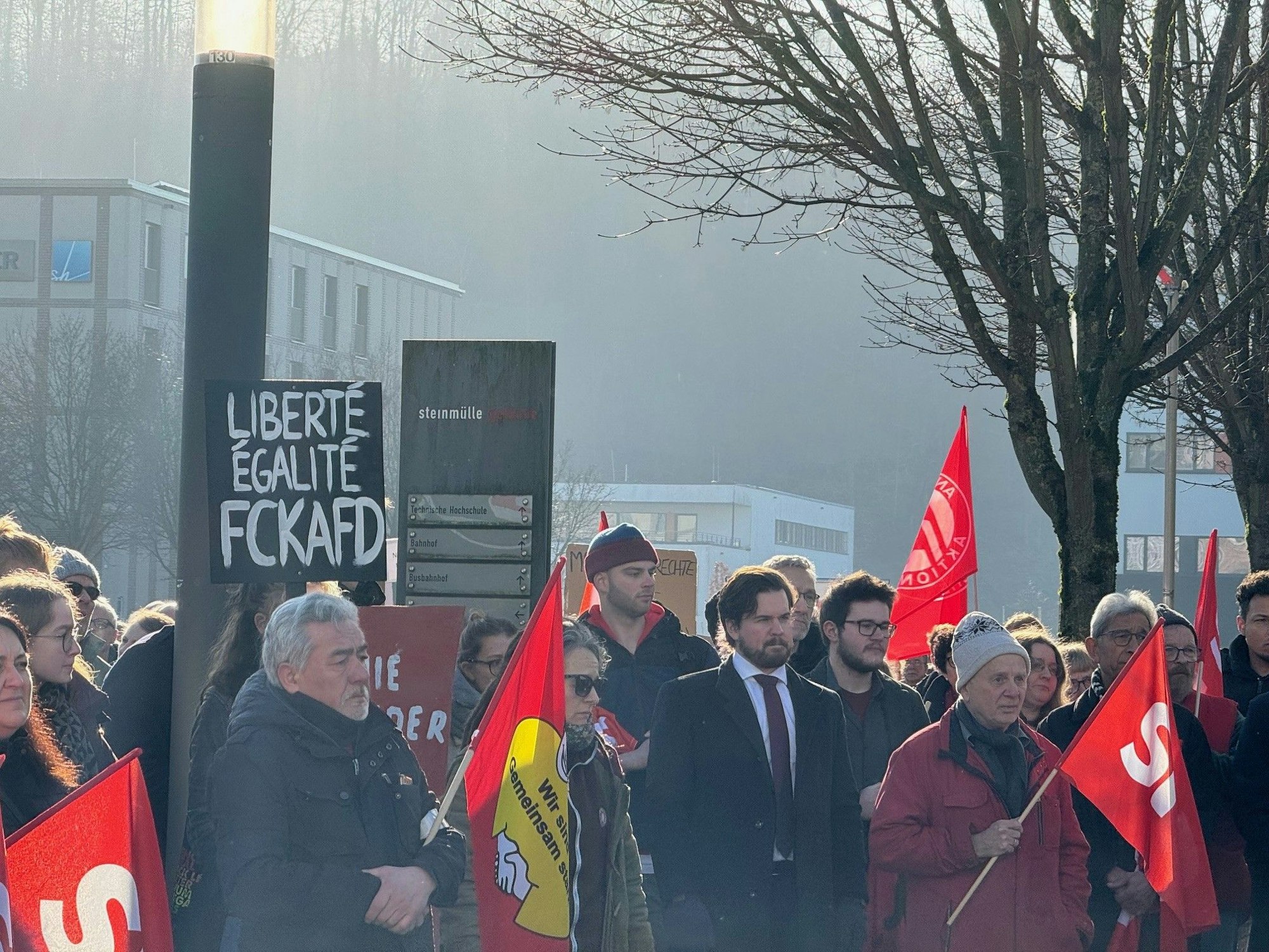 Menschen stehen mit Transparenten und Fahnen auf einem Platz.