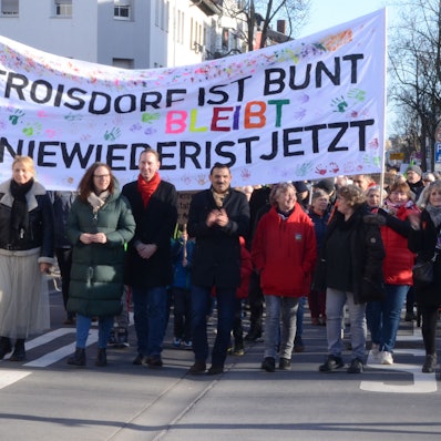Männer und Frauen laufen vor einem Transparent. „Troisdorf bleibt bunt“, steht darauf und „Nie wieder ist jetzt“.
