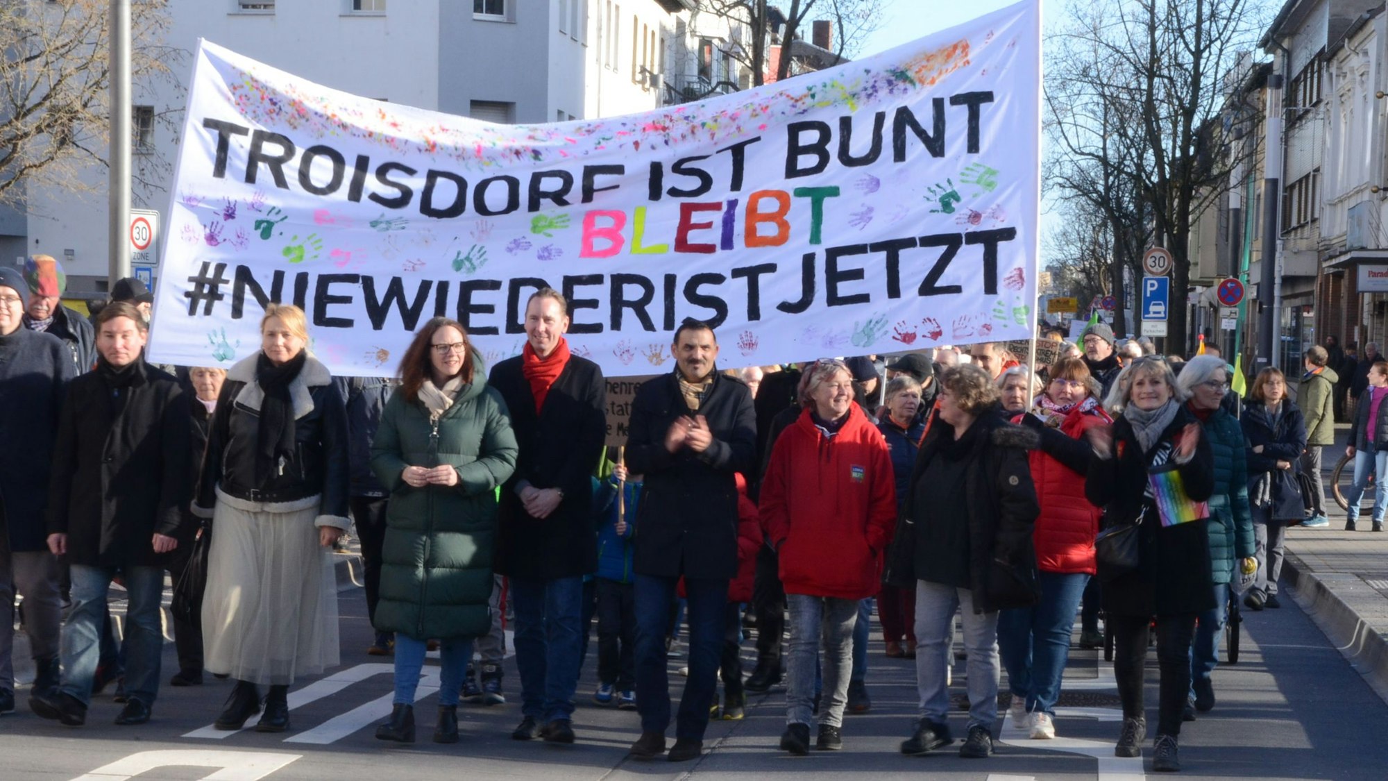 Männer und Frauen laufen vor einem Transparent. „Troisdorf bleibt bunt“, steht darauf und „Nie wieder ist jetzt“.