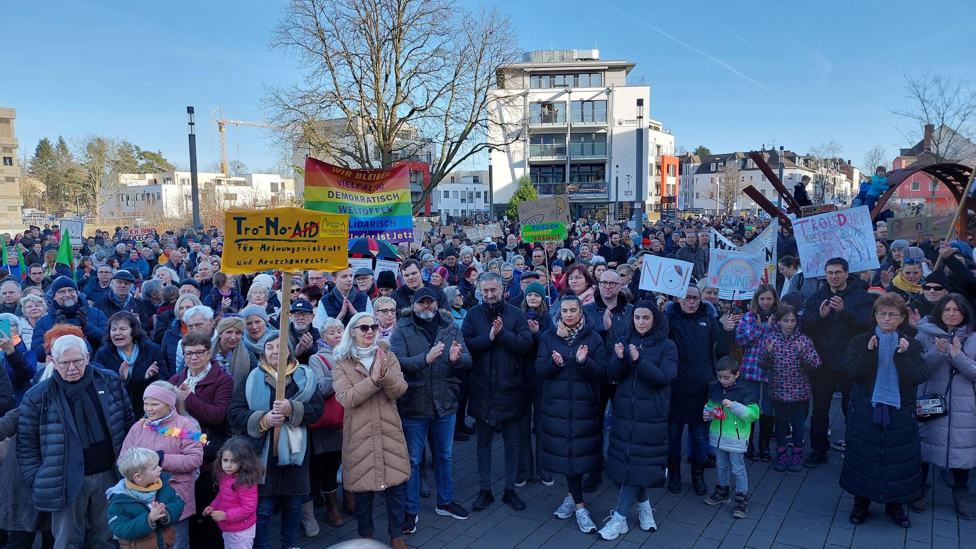 Eine große Menschenmenge steht auf einem Platz. Erwachsene und Kinder tragen Protestschilder.