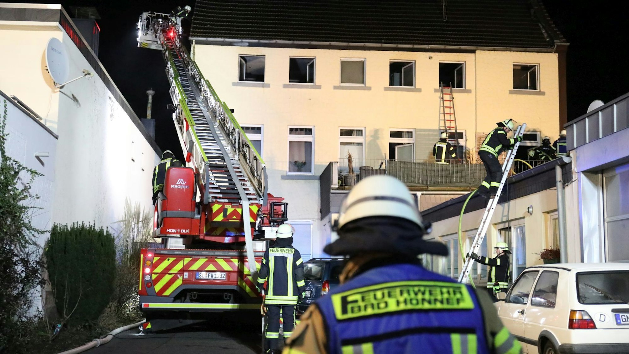 Einsatzkräfte der Feuerwehr steigen über eine Leiter auf das Flachdach eines Gebäudes; links steht eine Drehleiter