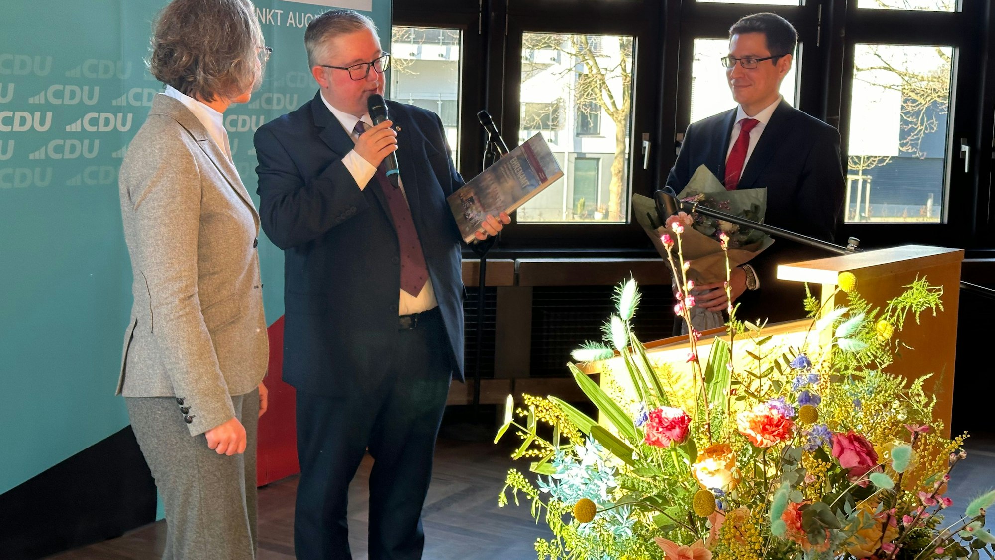 NRW-Ministerin Ina Scharrenbach bekam von Sascha Lienesch und Bürgermeister Max Leitterstorf das Jahresheft des Kreises geschenkt. Im Vordergrund des Bildes ein bunter Blumenstrauß.
