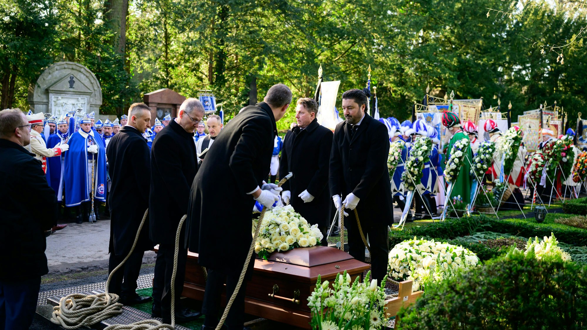 Ein Sarg wird in die Erde gelassen. Männer in blau-weißen Gardeanzügen stehen dahinter.