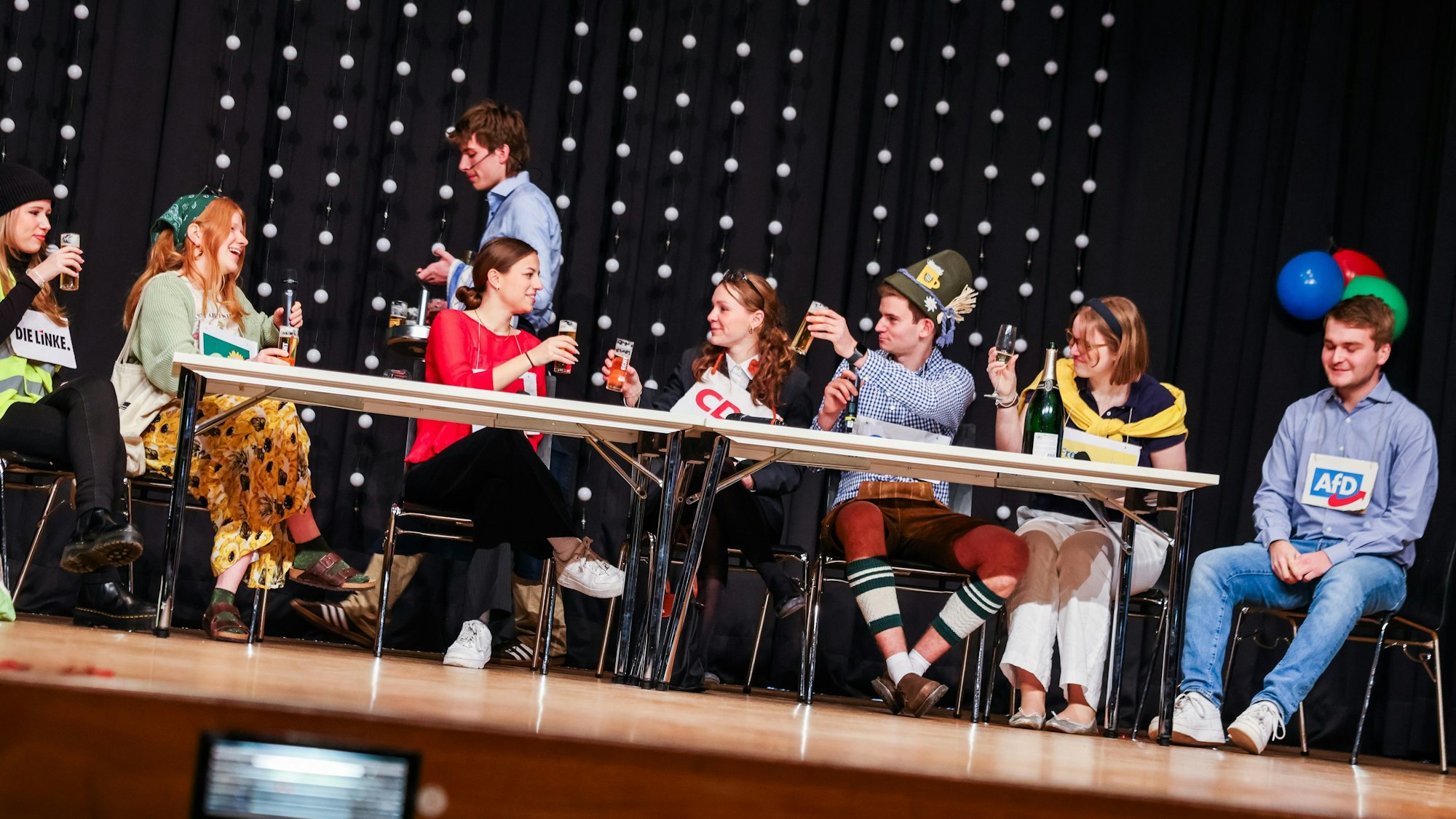 Junge Menschen sitzen verkleidet an einem Tisch auf einer Bühne.