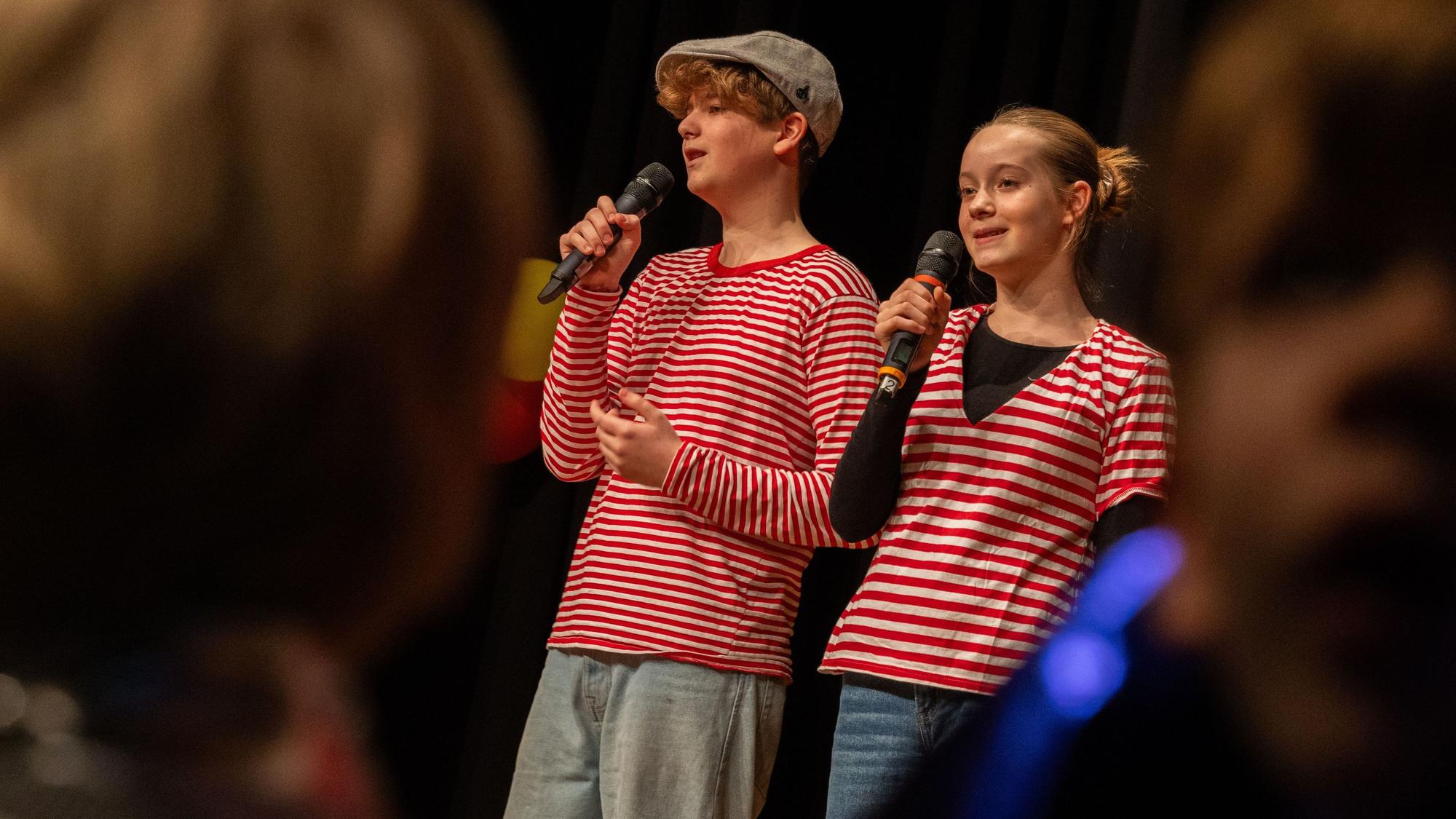 Zwei Kinder mit Mikros in rot-weißen Oberteilen.
