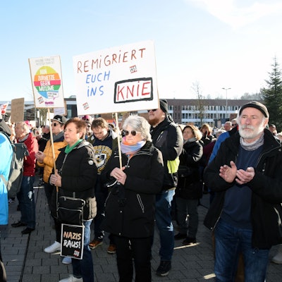 Hunderte Menschen stehen dicht gedrängt zusammen auf einem Platz, sie haben Fahnen und Schilder dabei.