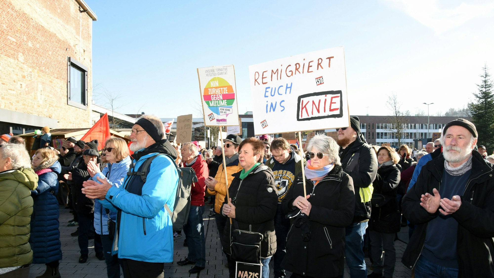 Hunderte Menschen stehen dicht gedrängt zusammen auf einem Platz, sie haben Fahnen und Schilder dabei.