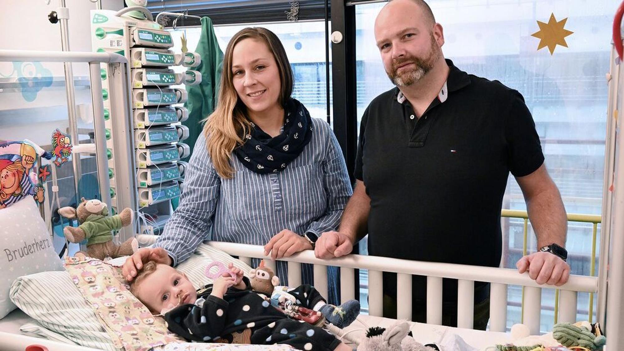 Ein Mann und eine Frau stehen am Krankenbett eines Säuglings.