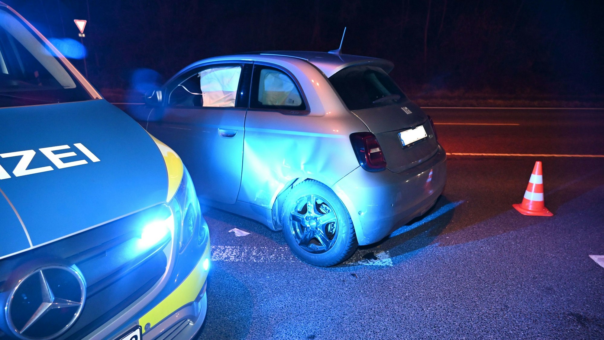 Wagen mit Delle an der Seite. Im Vordergrund ein Polizeiauto, daneben eine Pylone.
