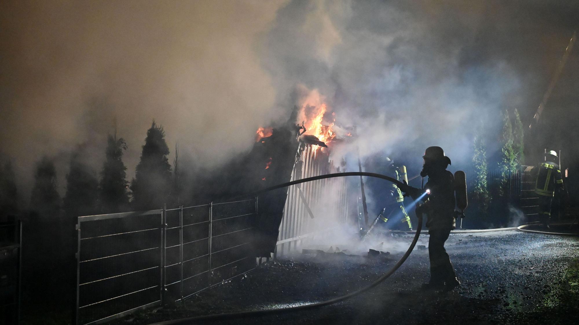 Feuerwehrleute mit Atemschutzausrüstung sind an den brennenden Überresten des dreieckigen Ferienhauses in Freilingen zu sehen.