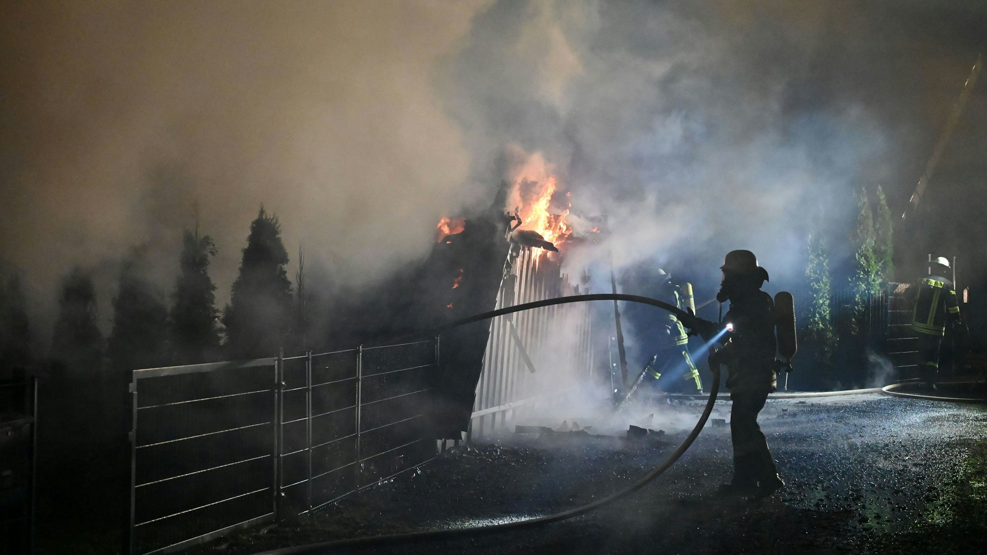 Feuerwehrleute mit Atemschutzausrüstung sind an den brennenden Überresten des dreieckigen Ferienhauses in Freilingen zu sehen.