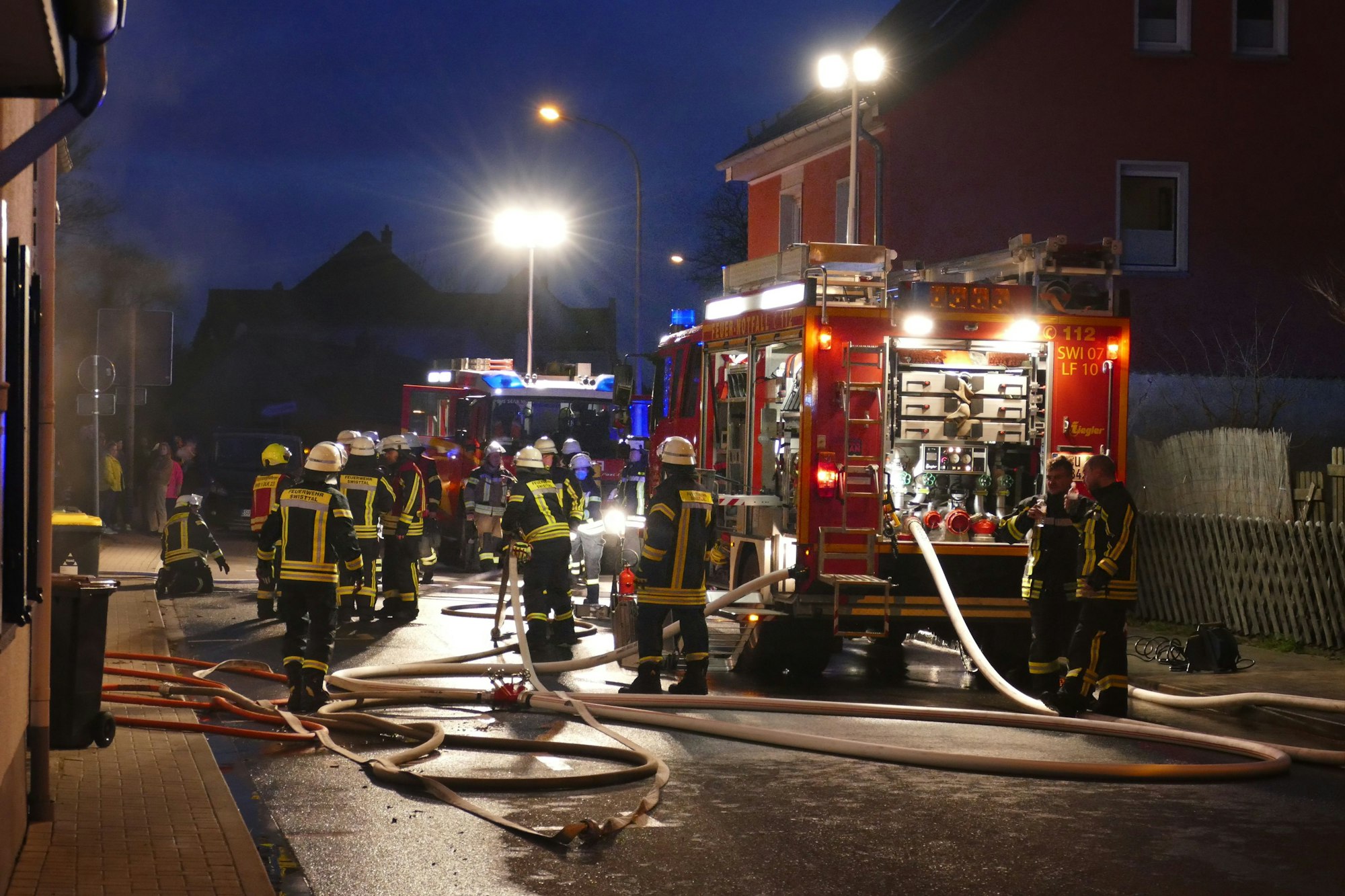 Feuerwehrautos und Feuerwehrleute auf einer Straße.