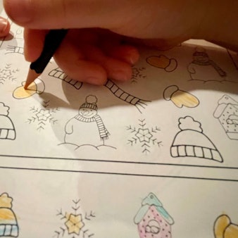 Das Bild zeigt die Hände eines Kindergartenkindes, das im Vorschulheft Bilder ausmalt.