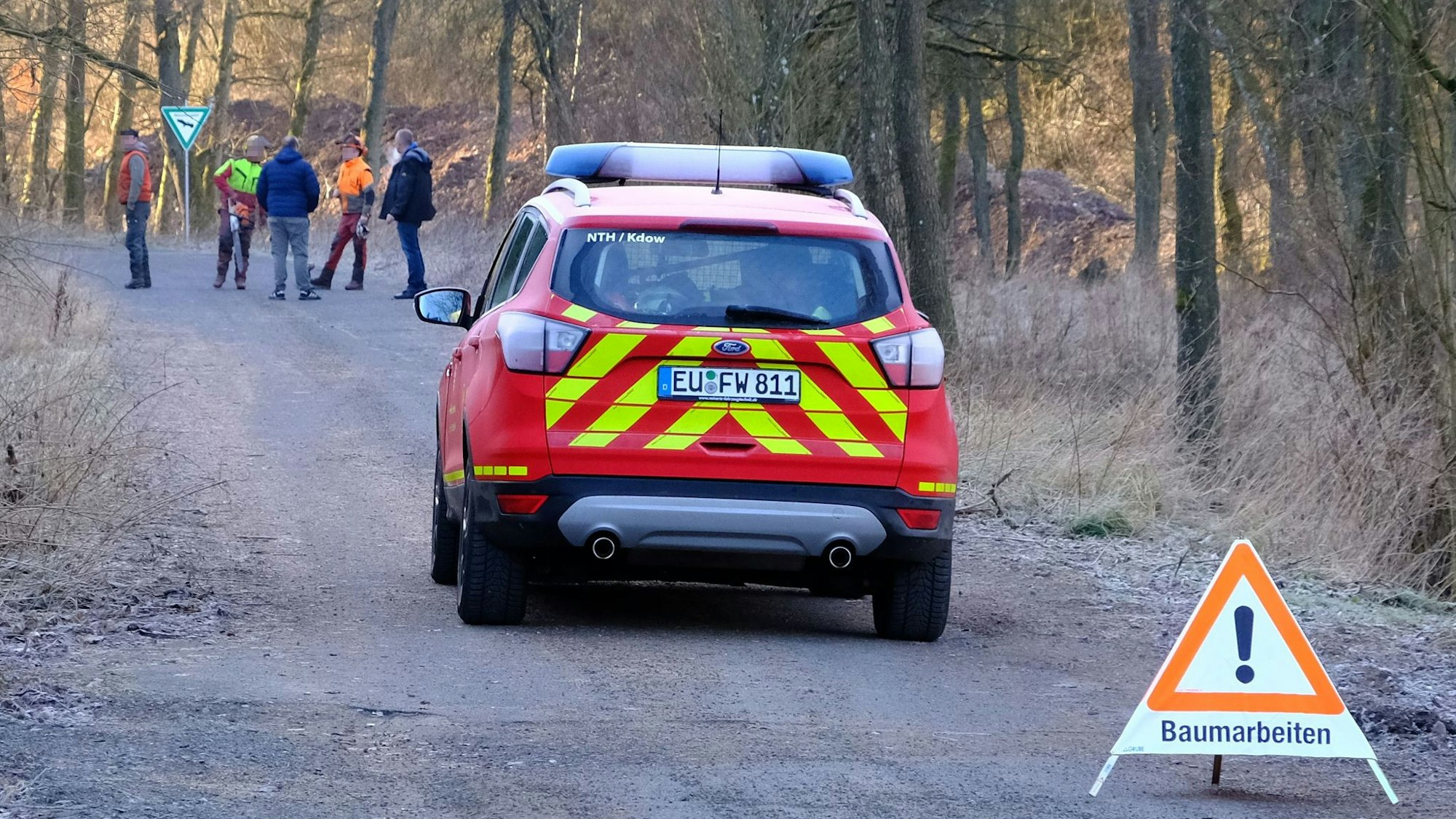 Hinter einem Warnschild mit der Aufschrift "Baumarbeiten" parkt ein Feuerwehrfahrzeug. Im Hintergrund sind einige Personen zu erkennen.