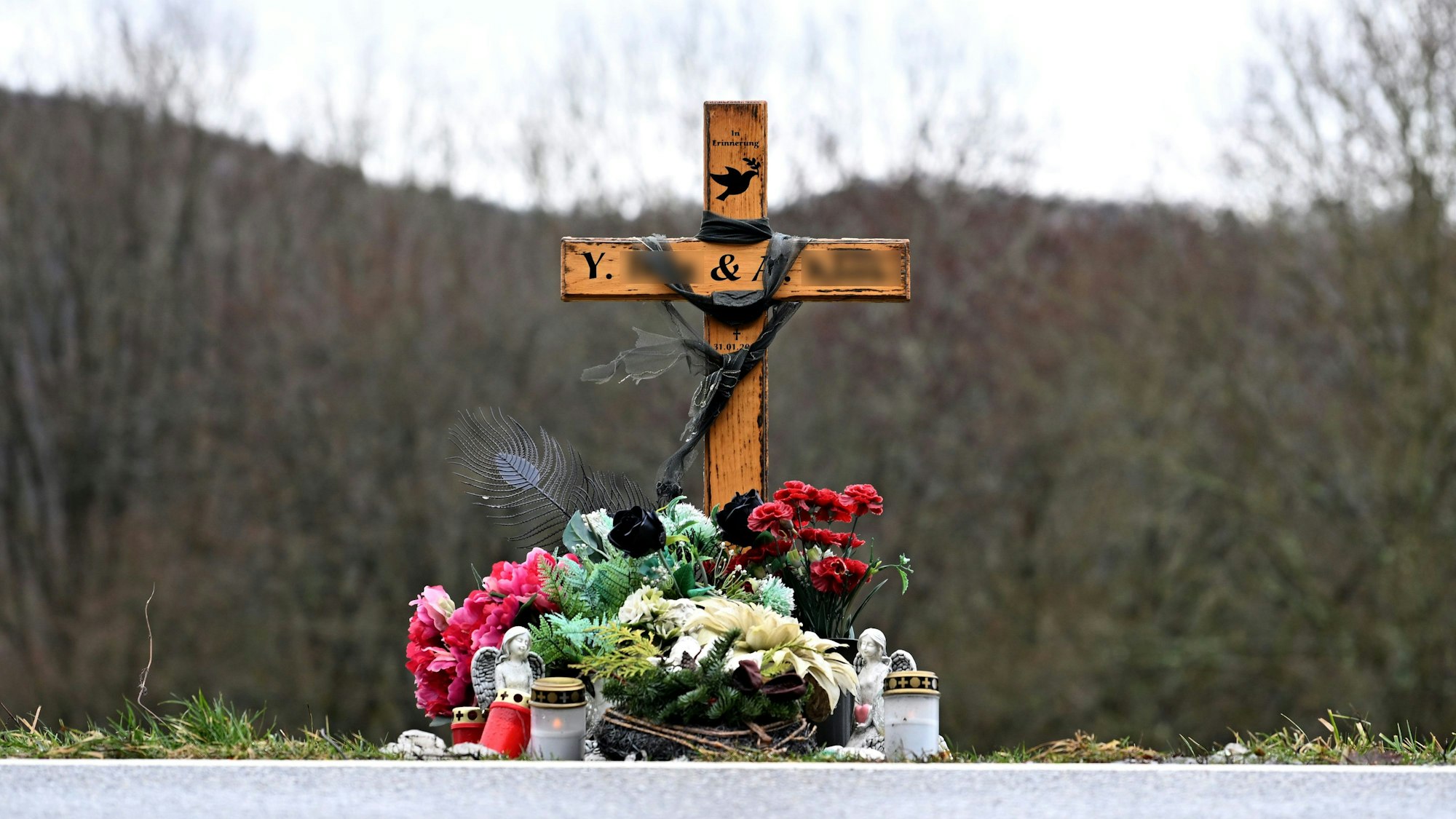 Ein mit Blumen und Schutzengeln geschmücktes Holzkreuz steht am Tatort.