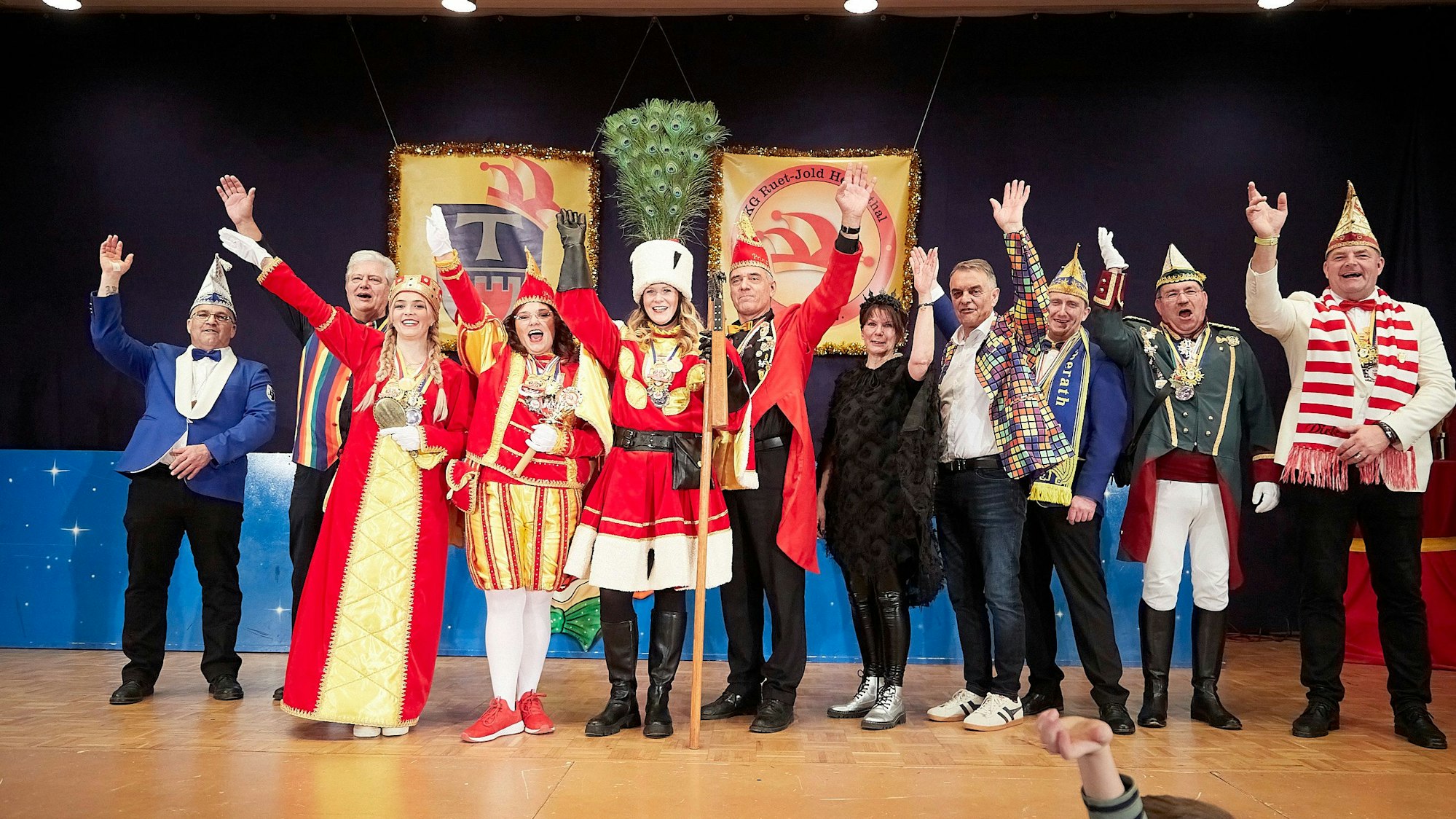 Kostümierte Karnevalistinnen, Karnevalisten und Politiker stehen in einer Reihe auf der Bühne und recken zum Alaaf-Rufe die Arme in die Höhe.