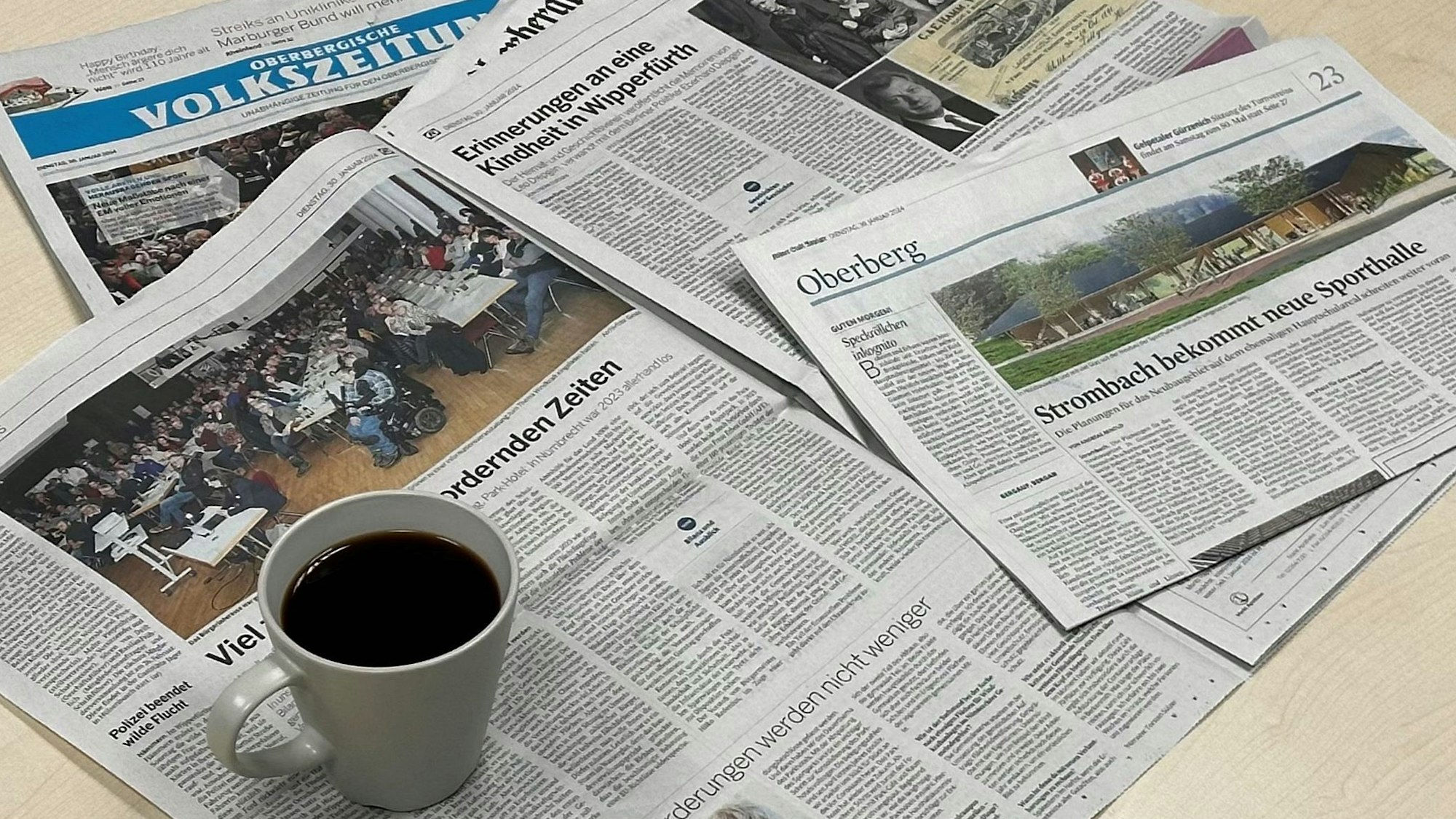 Zeitungsausgaben der Oberbergischen Volkszeitung und des Oberbergischen Anzeigers liegen auf einem Tisch. Darauf steht eine Tasse Kaffee.