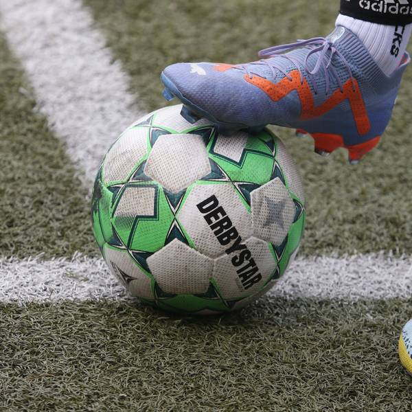 Auf der Linie liegt ein Fußball, der von einem Fuß mit Fußballschuh gehalten wird.