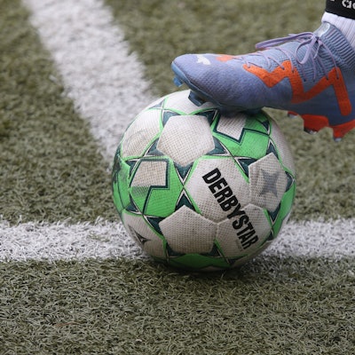 Auf der Linie liegt ein Fußball, der von einem Fuß mit Fußballschuh gehalten wird.