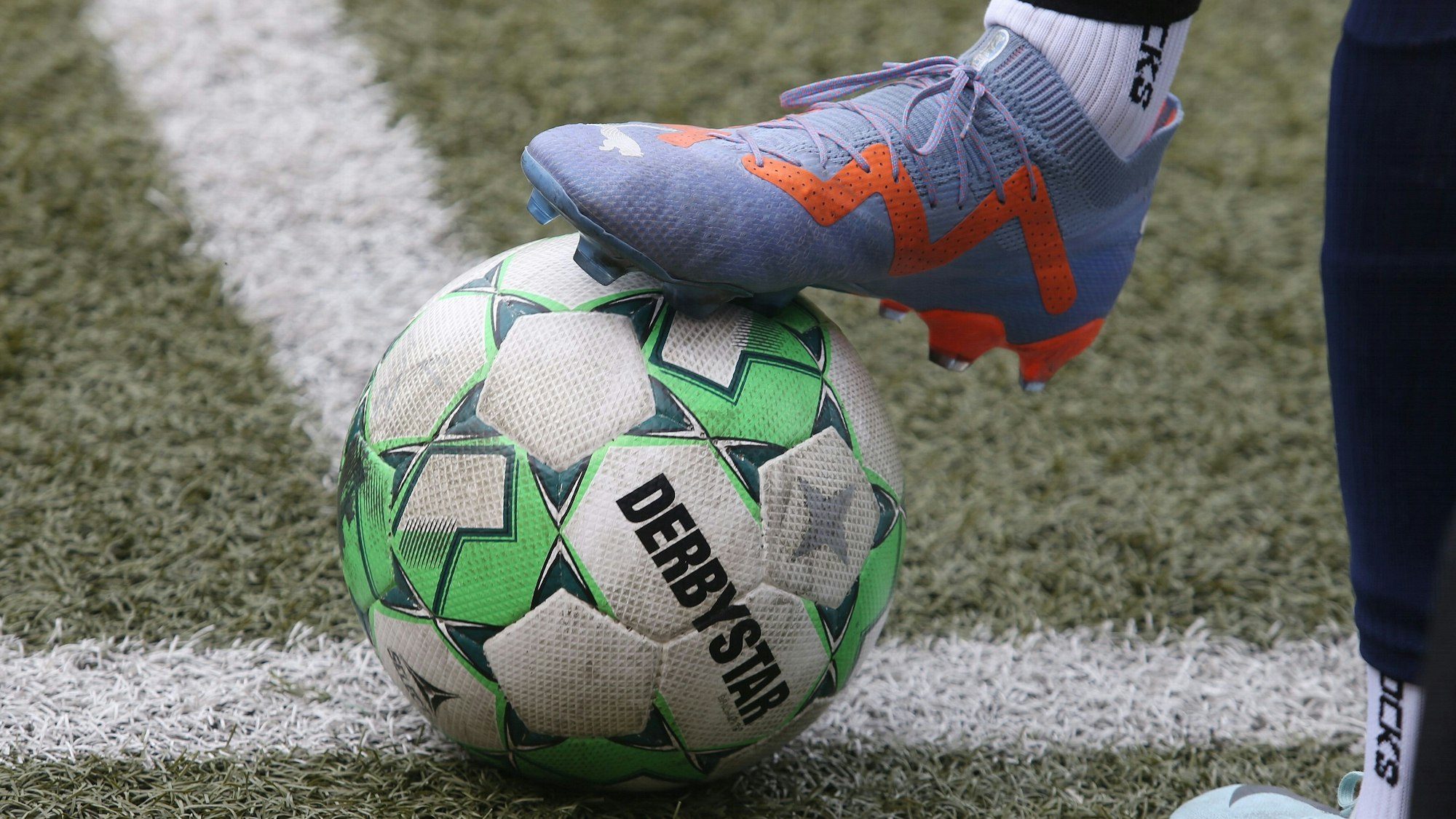 Auf der Linie liegt ein Fußball, der von einem Fuß mit Fußballschuh gehalten wird.