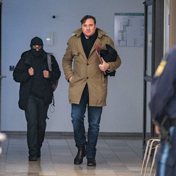 Der Windecker Pfarrer, der Sturmhaube und verspiegelte Brille trug, mit seinem Verteidiger im Trenchcoat auf dem Weg in den Verhandlungssaal des Landgerichts Deggendorf.