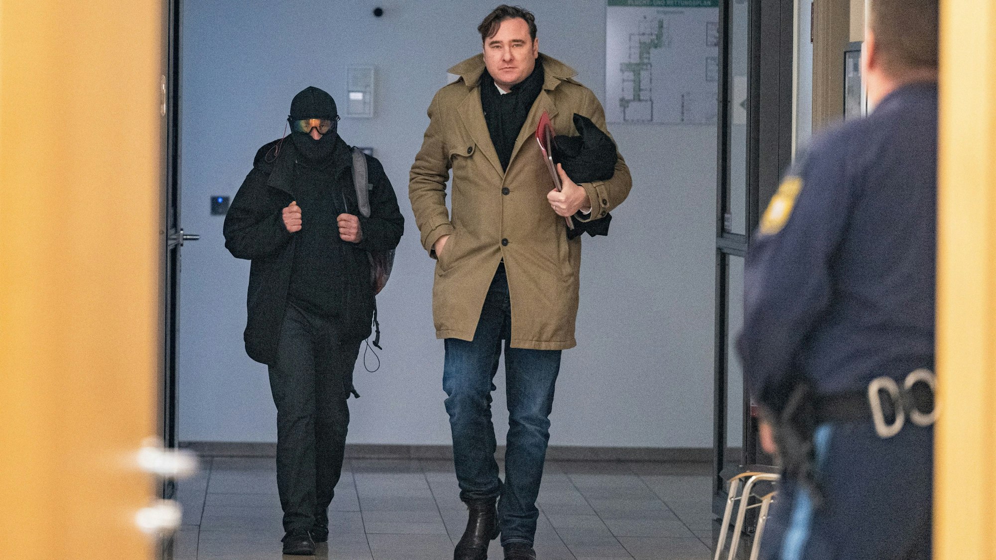Der Windecker Pfarrer, der Sturmhaube und verspiegelte Brille trug, mit seinem Verteidiger im Trenchcoat auf dem Weg in den Verhandlungssaal des Landgerichts Deggendorf.