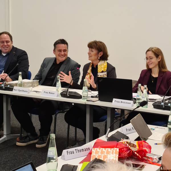 Drei Männer und zwei Frauen sitzen nebeneinander an einem Konferenztisch.