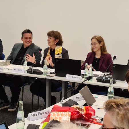 Drei Männer und zwei Frauen sitzen nebeneinander an einem Konferenztisch.
