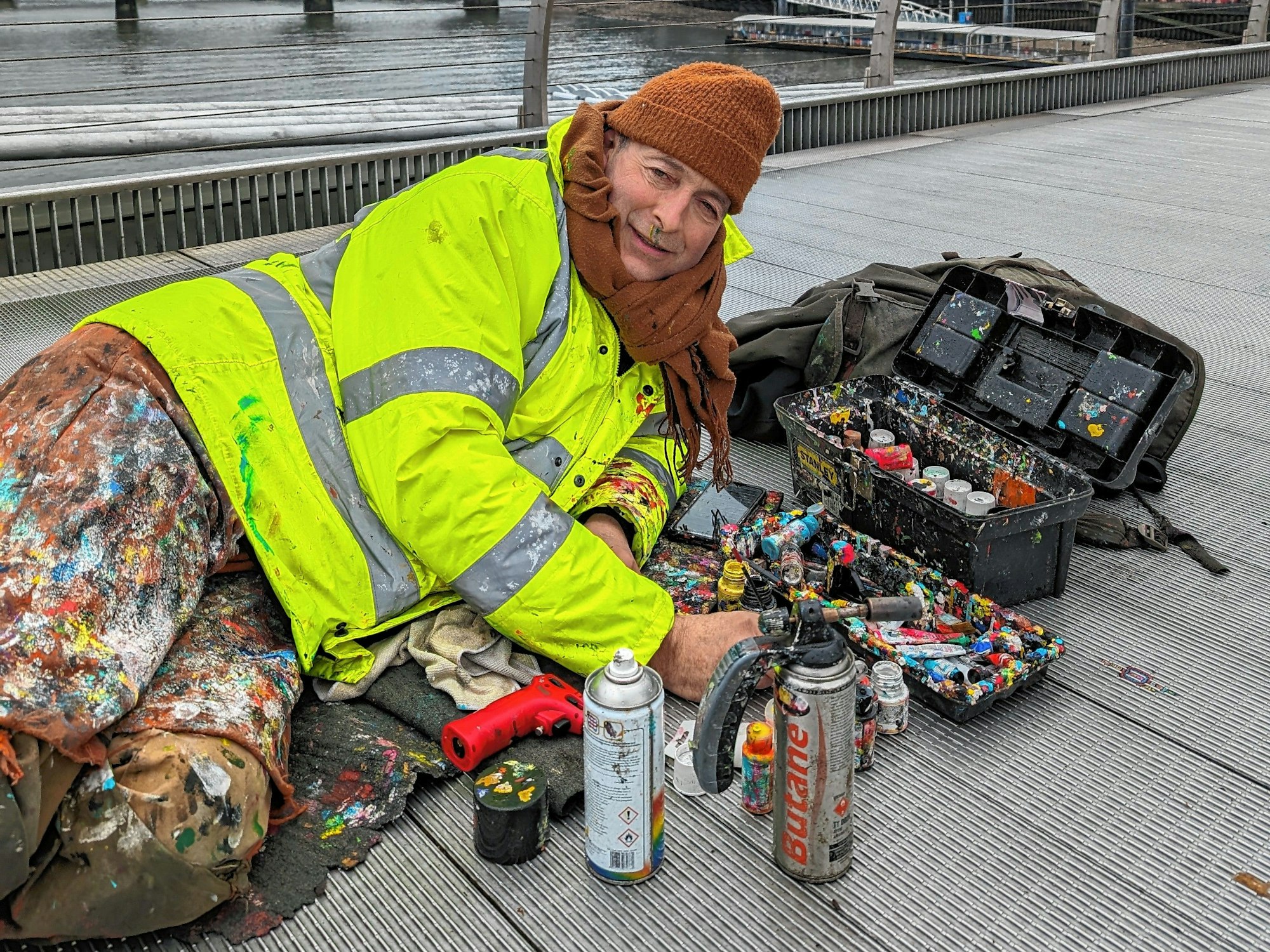 In seinem leuchtend orangen, mit Farbschichten überzogenen Industrieoverall mitten auf der Brücke oder auf Gehwegen der geschäftigen City wird der Künstler selbst zur Provokation.