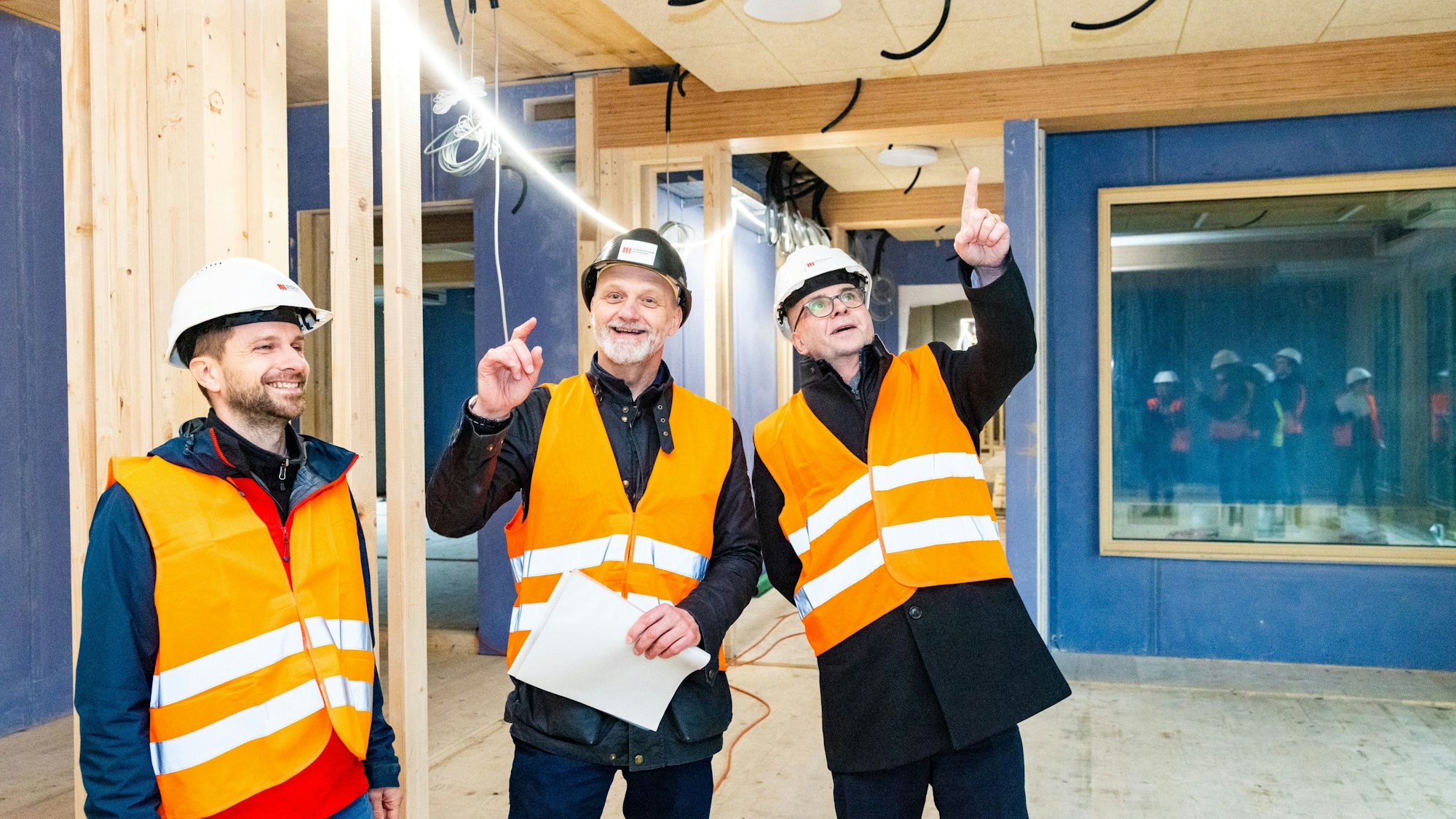 Drei Männer in Schutzwesten in einem Rohbau.