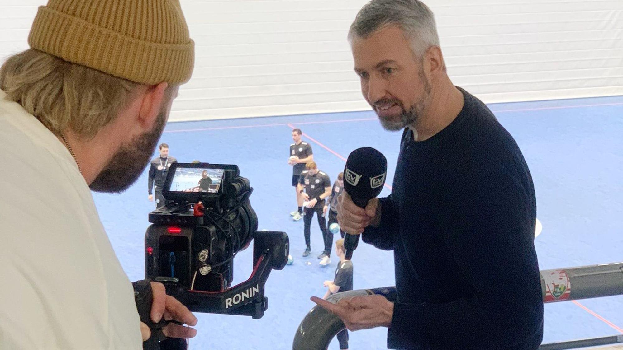 „TV Total“-Moderator Sebastian Pufpaff beim Handballtraining in der Schwalbe-Arena. Er spricht in ein Mikrofon und wird dabei von einem Kameramann gefilmt.