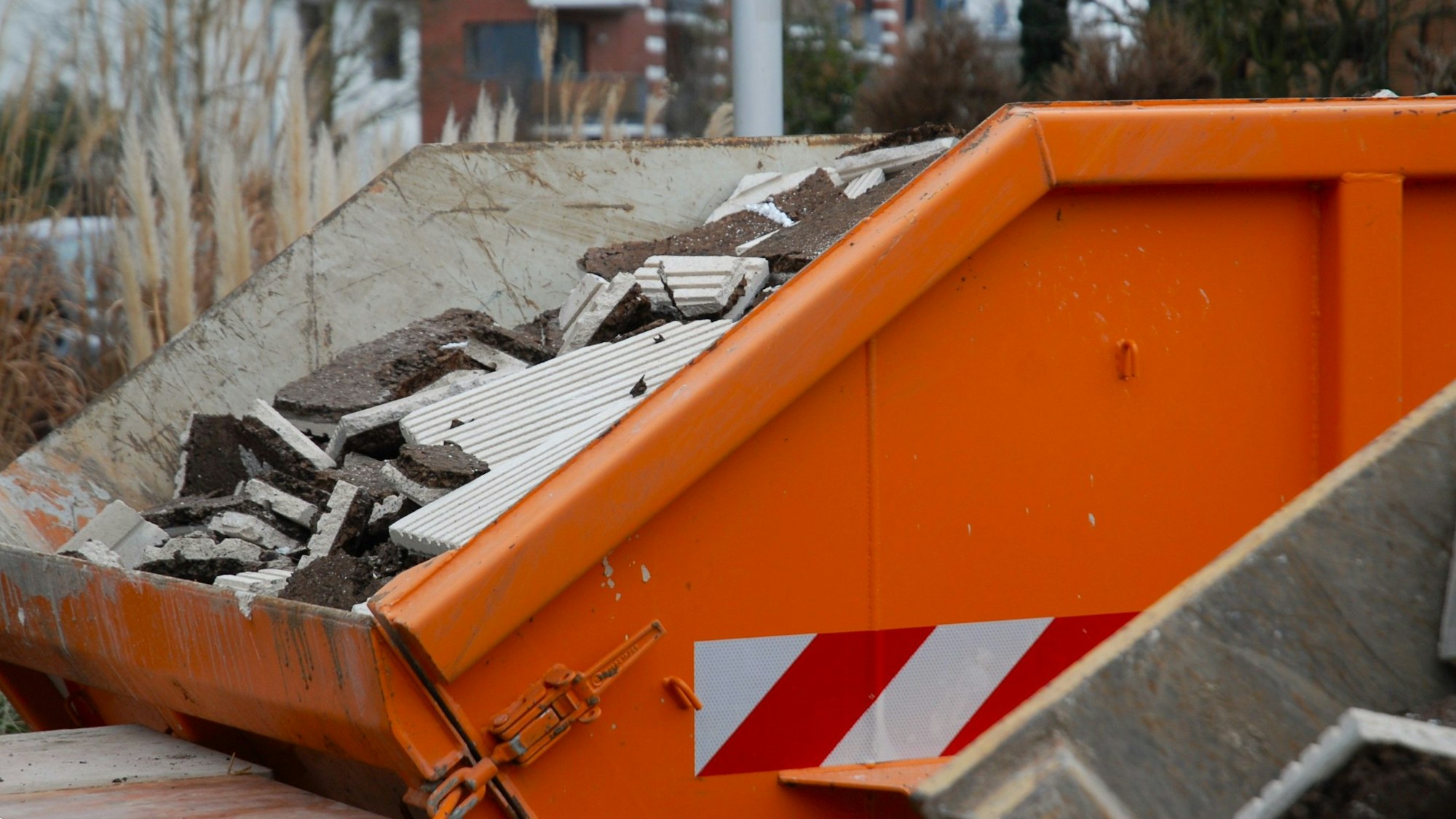 Zu sehen ist ein orangener Container mit Bauschutt.
