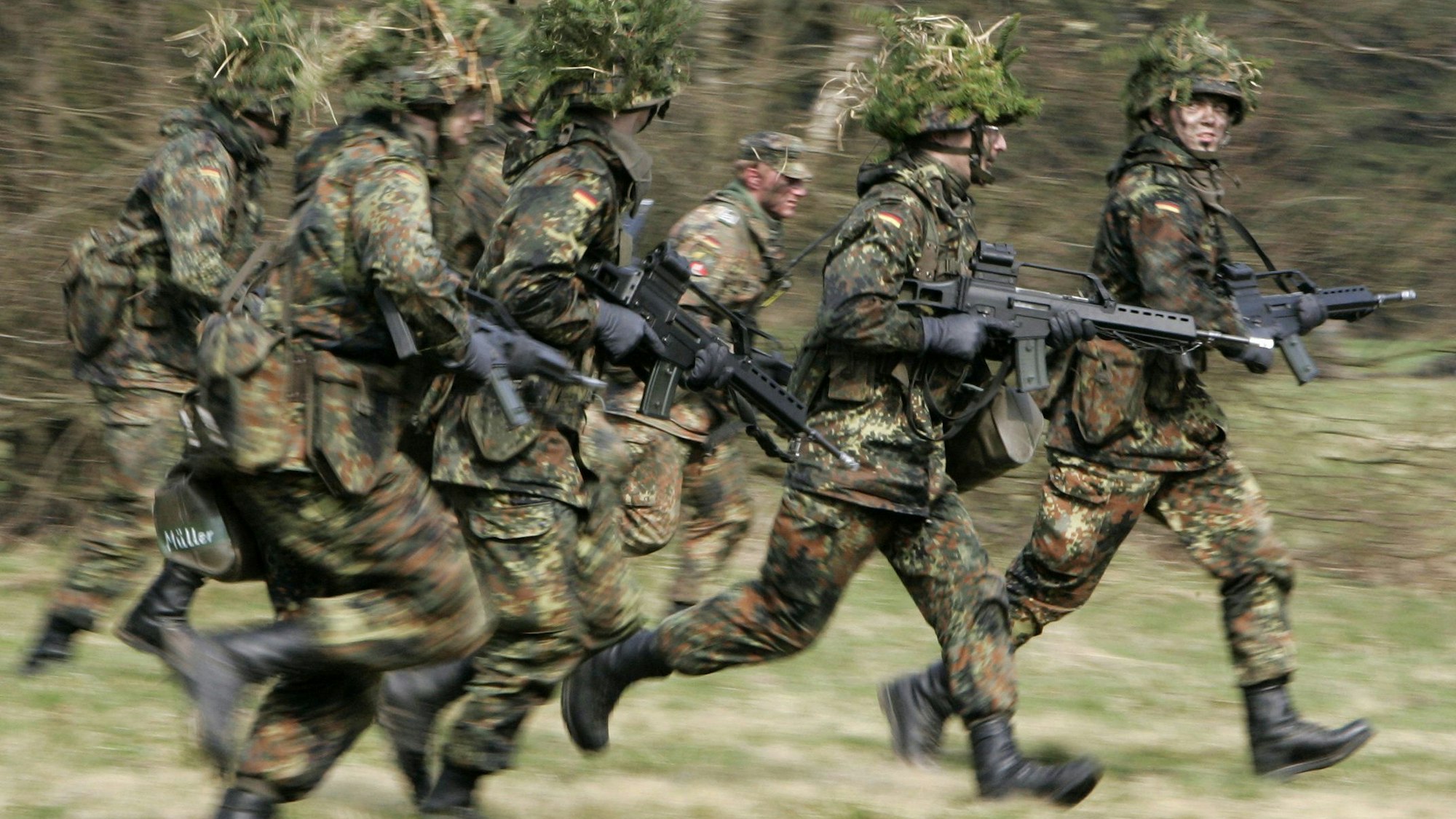 ARCHIV - 14.04.2005, Hessen, Schwarzenborn: Mit Blattwerk und Gras getarnte Wehrpflichtige rennen mit ihren Waffen im Rahmen ihrer Grundausbildung bei einer Übung über das freie Gelände der Knüll Kaserne in Schwarzenborn (Schwalm-Eder-Kreis). (zu dpa: «Reservistenverband für verpflichtendes Dienstjahr») Foto: +++ dpa-Bildfunk +++