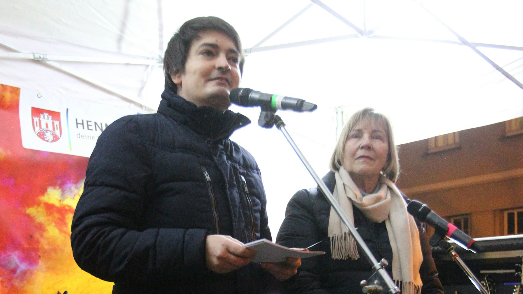 Ein Mann spricht in ein Mikrofon. Neben ihm steht eine Frau.